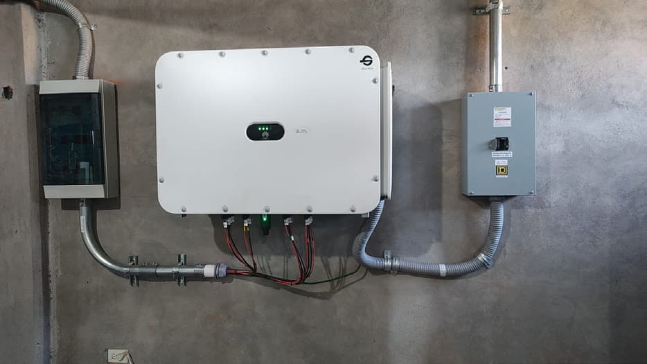 Inversor Huawei montado en muro, con canalización metálica, tablero de protección y desconectador instalados a cada lado.